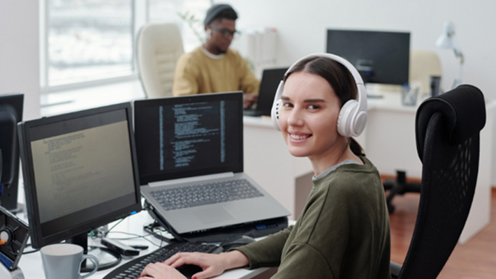 Junge Frau mit Kopfhörern sitzt am Arbeitsplatz und programmiert.