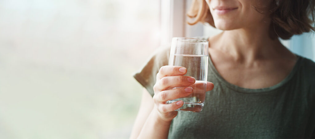 Eine Frau mit einem Wasserglas lächelt, denn unser Coaching unterstützt sie dabei, ihre gesundheitliche Situation zu festigen und neue berufliche Perspektiven zu entwickeln.